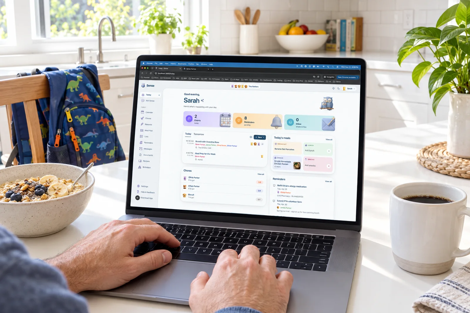 A laptop on a kitchen table showing the Sense web app Today view, with a bowl of oatmeal, coffee, and a kid's backpack on the chair